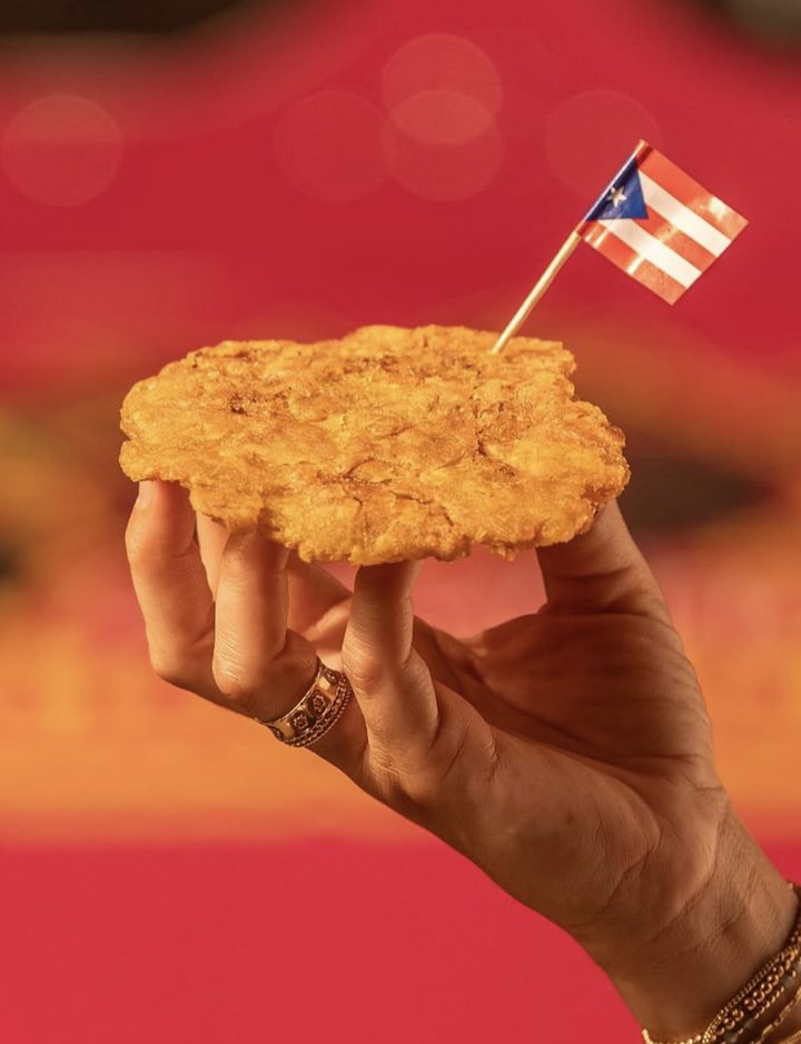 A golden tostón held up with a Puerto Rican flag toothpick